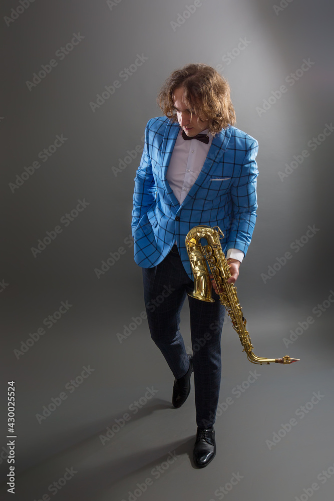 Fototapeta premium Full-length studio portrait of a young musician guy holding a saxophone.