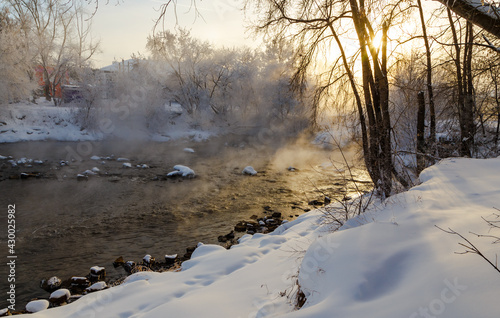 The rays of the sun break through the winter branches of the trees on the bank of the river with fog. the bitter cold of minus 30 degrees Celsius. photo