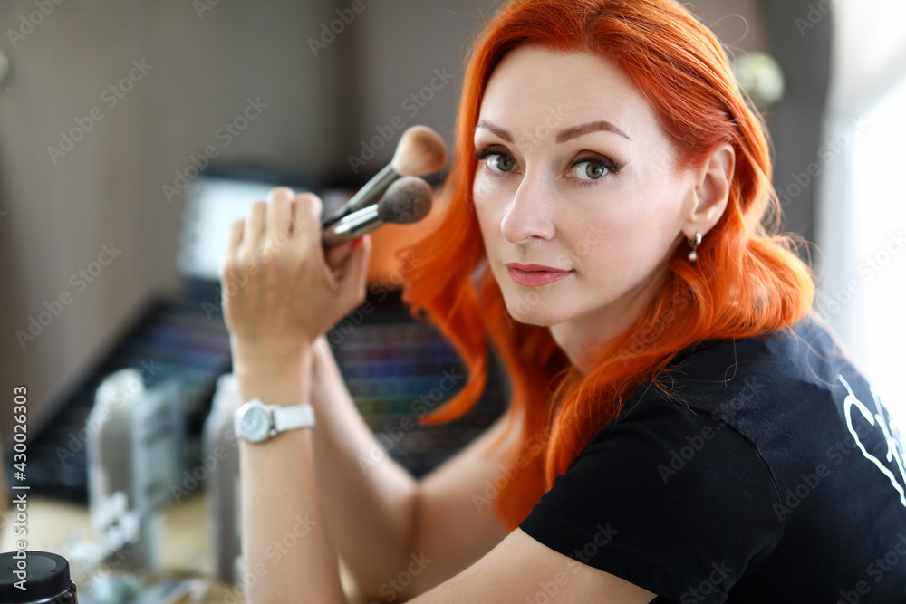 Fototapeta premium Beautiful redhead woman holding new makeup brushes