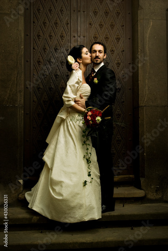 Gorgeous wedding couple (bride and groom) standing on staircase in front of historical church doorway and kissing.