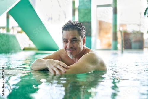 Smiling man relaxing in indoor swimming pool. Concepts of spa, wellness, vacation.