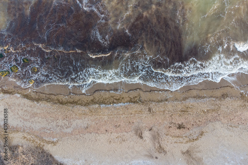 Steep sea shore and surf. Sea water muddy with sand after storm and algae. Aerial view.
