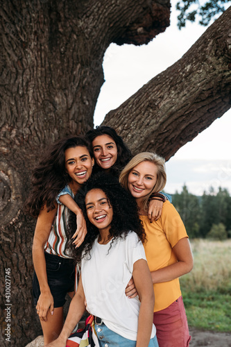Photo Group of young diverse women standing in front of a big tree and looking at came