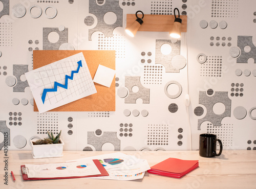 a comfortable workplace and a note board. notebook, charts and a cup are on the table