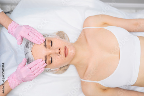 Closeup of beautician hands in gloves touching young woman's face. Plastic surgery concept. Facial beauty and massage. Portrait of beautiful blonde female with perfect makeup and soft smooth skin. 