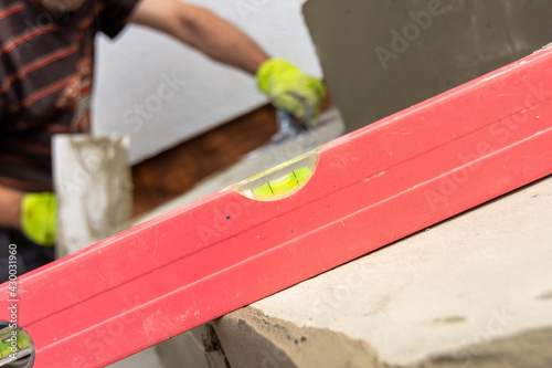Detail of a spirit level and water bubbles for measuring the flatness of the stair surface when laying paving. Working man with trowel in background.