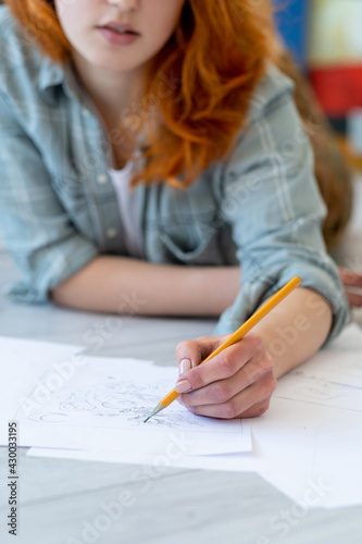 Drawing hobby. Art school. Creative skill talent. Left-handed red-haired female artist sketching with pencil in hand on white paper on light blur background.