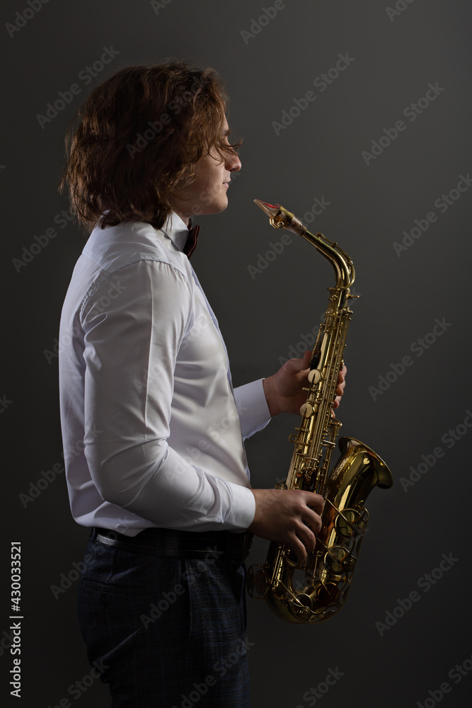 Fototapeta premium Studio portrait of young cool man with saxophone on dark background.