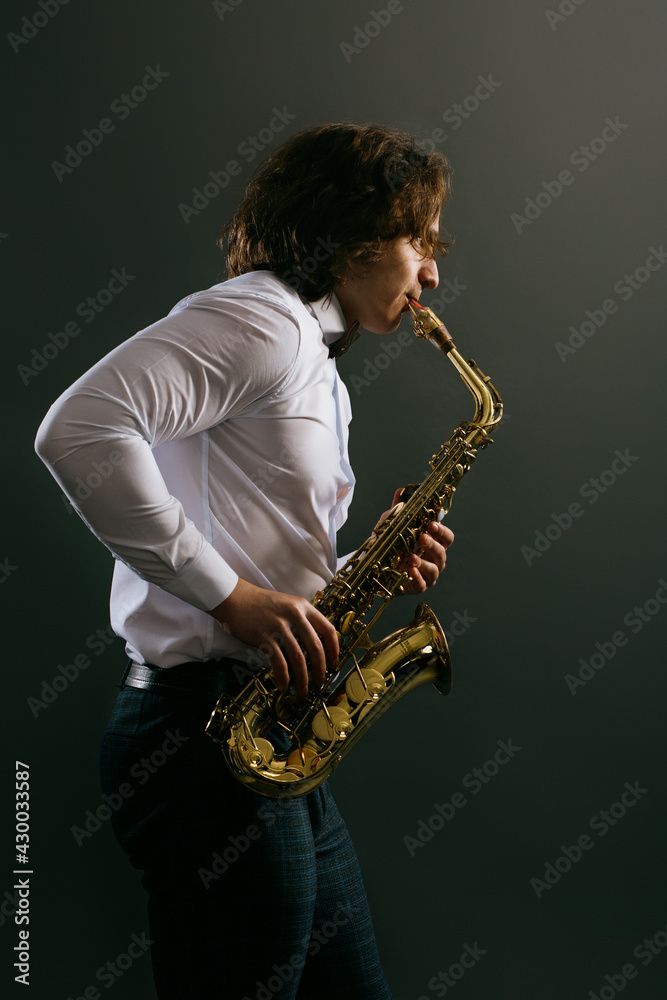 Fototapeta premium Studio portrait of young cool man with saxophone on dark background.