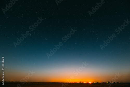 Night Starry Sky Over Yellow Sunset Or Sunrise Lights. Night Glowing Stars. Dark Night Starry Sky Over Ground In Warm Yellow Colors. Copyspace Space Abstract Landscape Background