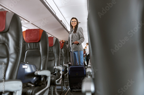 Happy caucasian female passenger with luggage in airplane salon