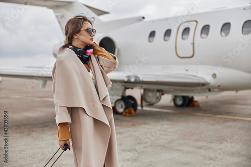 Fototapeta Mature business woman in coat near her jet in airport