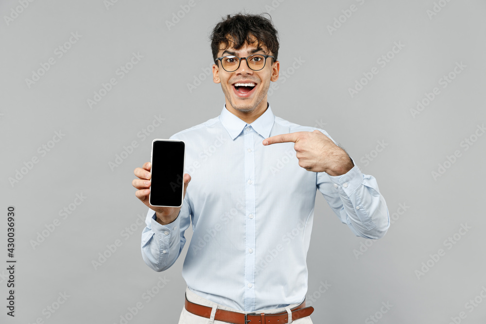 Young employee business latin man corporate lawyer in classic white shirt glasses point index finger on mobile cell phone with blank screen workspace area isolated on grey background studio portrait Young employee business latin man corporate lawyer in classic white shirt glasses point index finger on mobile cell phone with blank screen workspace area isolated on grey background studio portrait