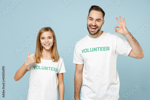 Two young friends couple teen girl man wears white t-shirt green title volunteer show ok fingers gesture isolated on pastel blue color background. Voluntary free team work help charity grace concept.