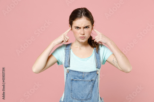 Young sad caucasian woman in denim clothes blue t-shirt cover ears with hands fingers do not want to listen scream isolated on pastel pink color background studio portrait. People lifestyle concept