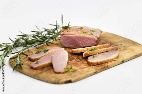 Smoked duck sliced with herbs on a wooden background.