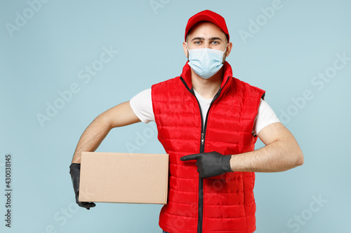 Delivery guy employee man in red cap white t-shirt vest uniform sterile face mask gloves work courier service on lockdown covid19 flu virus hold empty cardboard box isolated on pastel blue background