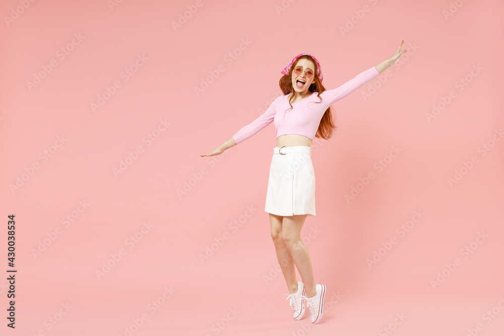 Full length young fun smiling happy caucasian woman 20s in rose clothes bandana glasses leaning back stand on toes dancing with outstretched hands isolated on pastel pink background studio portrait Full length young fun smiling happy caucasian woman 20s in rose clothes bandana glasses leaning back stand on toes dancing with outstretched hands isolated on pastel pink background studio portrait