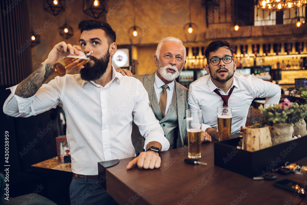 Obraz premium Three businessmen cheering while watching football match in a cafe bar.