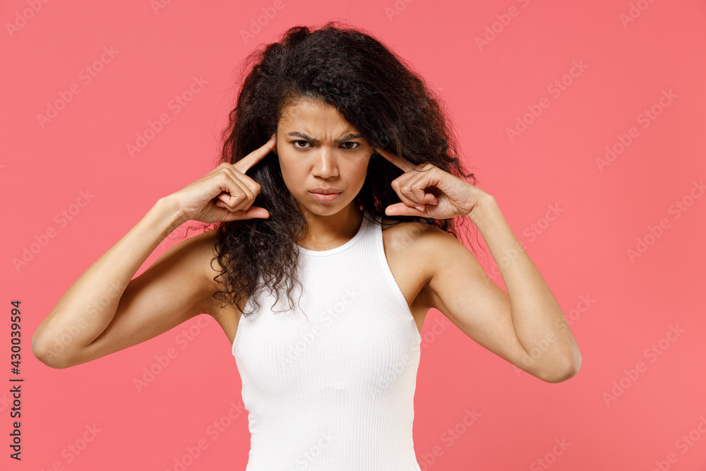 Naklejka premium Young disappointed depressed iritated nervous sad african american woman 20s wearing casual white tank shirt cover ears with fingers hands isolated on pink color background. People lifestyle concept.