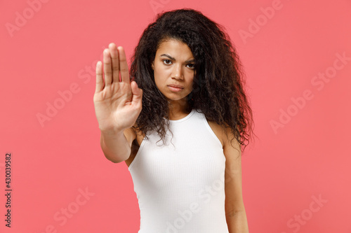 Young serious strict sad angry frowning confident african american woman 20s wear casual white tank shirt doing stop palm gesture refusing say no isolated on pink background. People lifestyle concept.