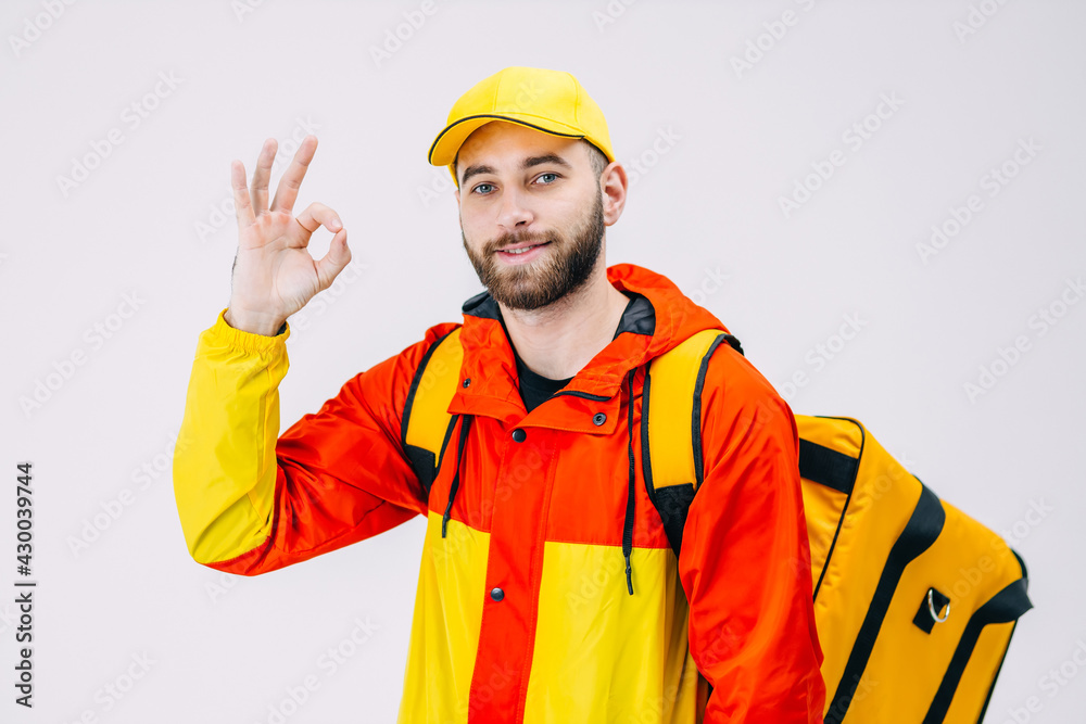 Young bearded man holding a take-away backpack makes an OK sign with his fingers, smiling friendly and gesturing a great symbol. Young bearded man holding a take-away backpack makes an OK sign with his fingers, smiling friendly and gesturing a great symbol.