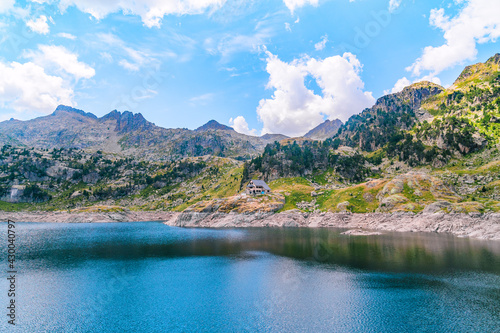 Mountainous landscape with a beautiful blue lake and a mountain refuge in a green alpine valley on a sunny summer day. Concept of summer vacations and mountain trip.