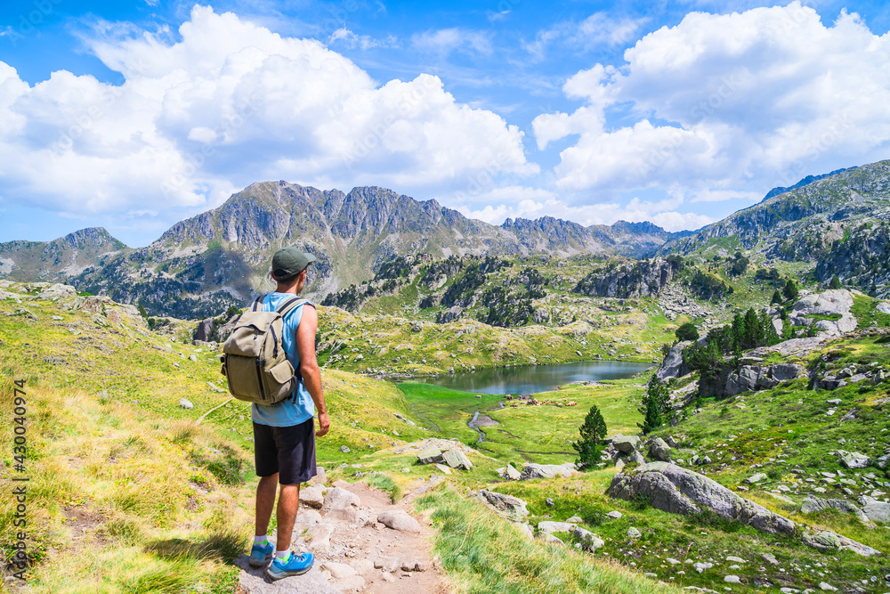 Young man with a bag standing on an alpine mountain trail with a lake.