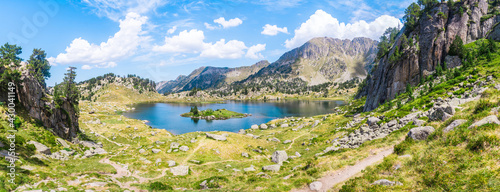 Panoramic mountain lake surrounded by mountains with green grass on a lovely sunny summer day. Concept of mountain trip and summer vacations. Circo Saboredo, Aran Valley-Pyrenees, Catalonia, Spain.