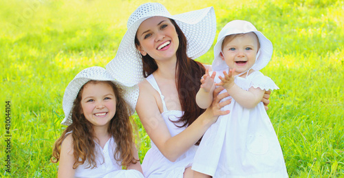 Portrait of happy smiling mother with two daughters children wearing a summer straw hats on the grass in a park © rohappy