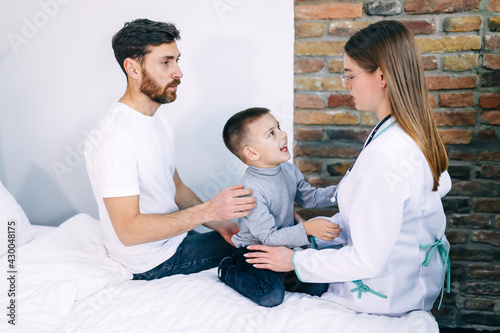 pediatrician woman consulting man with little son sitting on papa's lap, listening to doctor, children health care concept