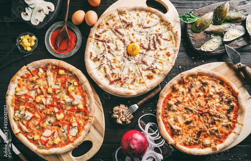 Variety of meat pizzas with sausage, ham, prosciutto, salami, chicken fillet, pepperoni, mussels, cheese, tuna fish, vegetables on dark background. Fast food lunch for picnic company, top view, toning
