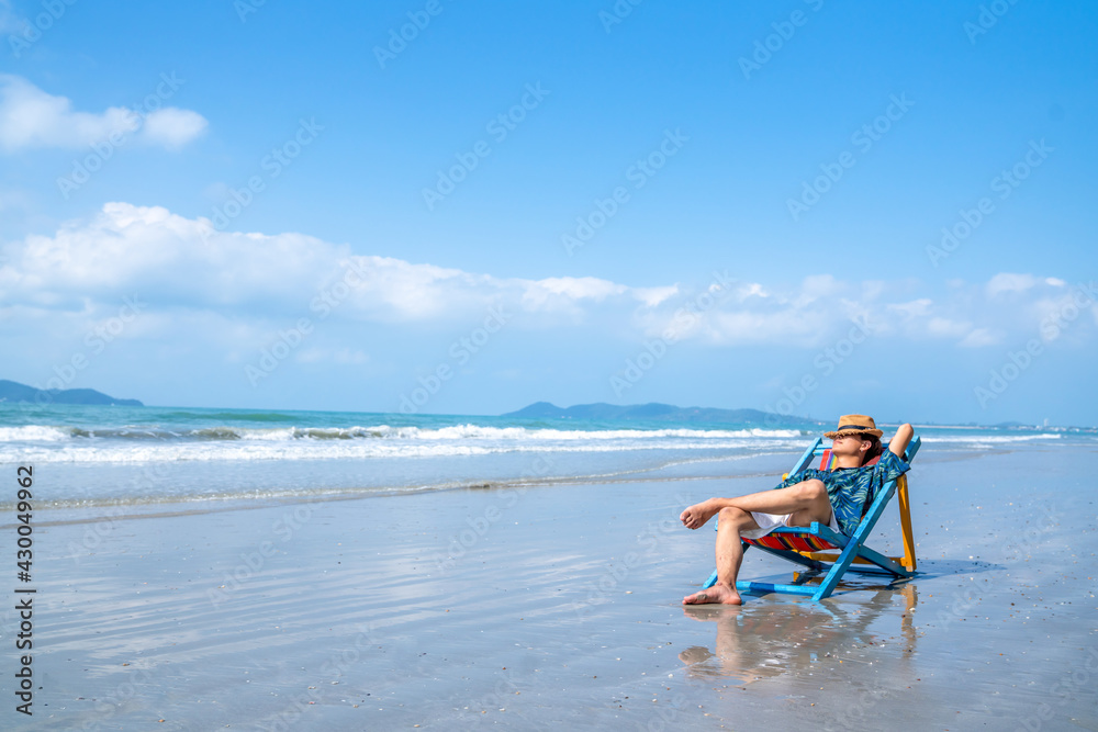 Asian man resting on beach chair at tropical beach. Happy guy sunbathing or nap on sunbed by the sea in sunny day. Young man relax and enjoy beach outdoor activity lifestyle on summer holiday vacation Asian man resting on beach chair at tropical beach. Happy guy sunbathing or nap on sunbed by the sea in sunny day. Young man relax and enjoy beach outdoor activity lifestyle on summer holiday vacation