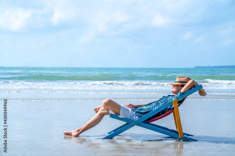 Asian man resting on beach chair at tropical beach. Happy guy