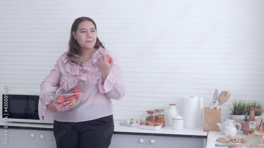 Young asian woman fat standing eating apple in the kitchen at home, fruits for healthy, dieting and weight loss, female with overweight and nutrition for health care, plus size, lifestyles concept. Young asian woman fat standing eating apple in the kitchen at home, fruits for healthy, dieting and weight loss, female with overweight and nutrition for health care, plus size, lifestyles concept.