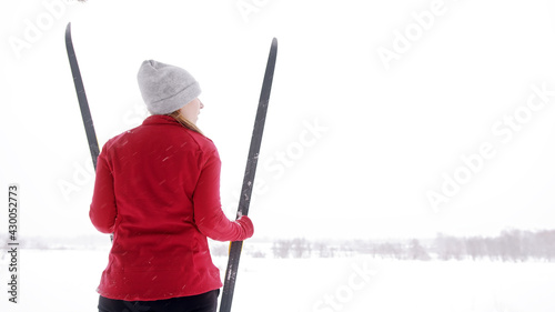 Woman in red winter jacket standing and holding skis on the mountain covered in snow. High quality photo