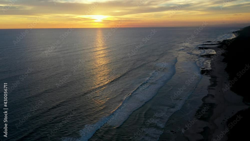 Aerial of beautiful sunset reflecting in the water with waves and surfers in the pacific ocean in Tamarindo, Costa Rica. Tilting up and reveal shot. Aerial of beautiful sunset reflecting in the water with waves and surfers in the pacific ocean in Tamarindo, Costa Rica. Tilting up and reveal shot.