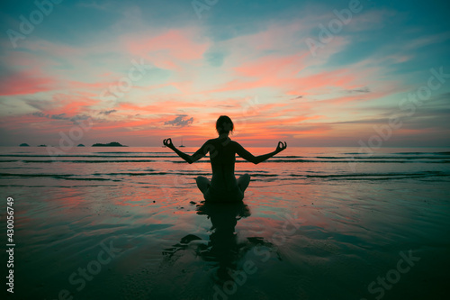 A woman practicing yoga on the beach during surreal sunset.