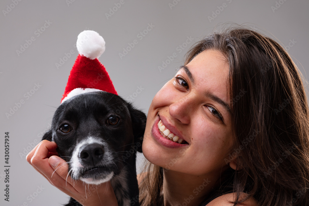 Cute little dog wearing a Santa hat with a smiling young woman Cute little dog wearing a Santa hat with a smiling young woman