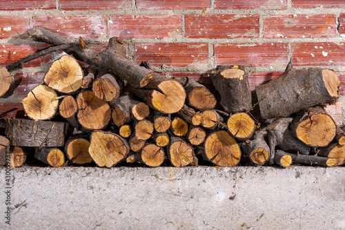 Firewood stacked on concrete and a brick wall.The photograph is a horizontal shot.