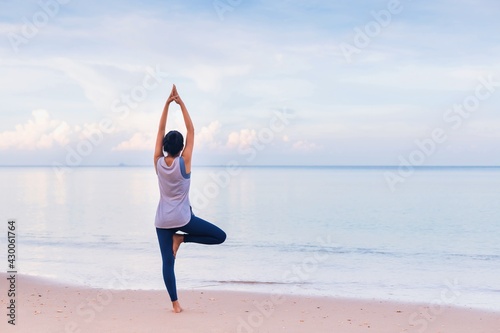 Asian woman warm up and play yoga exercise on the beach by the sea at morning sky background.