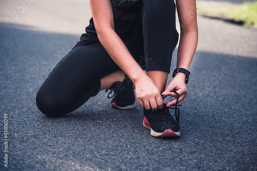 Young woman tying running shoe for prepare jogging on asphalt way in the park, female working out outdoor, wellness healthy concept.