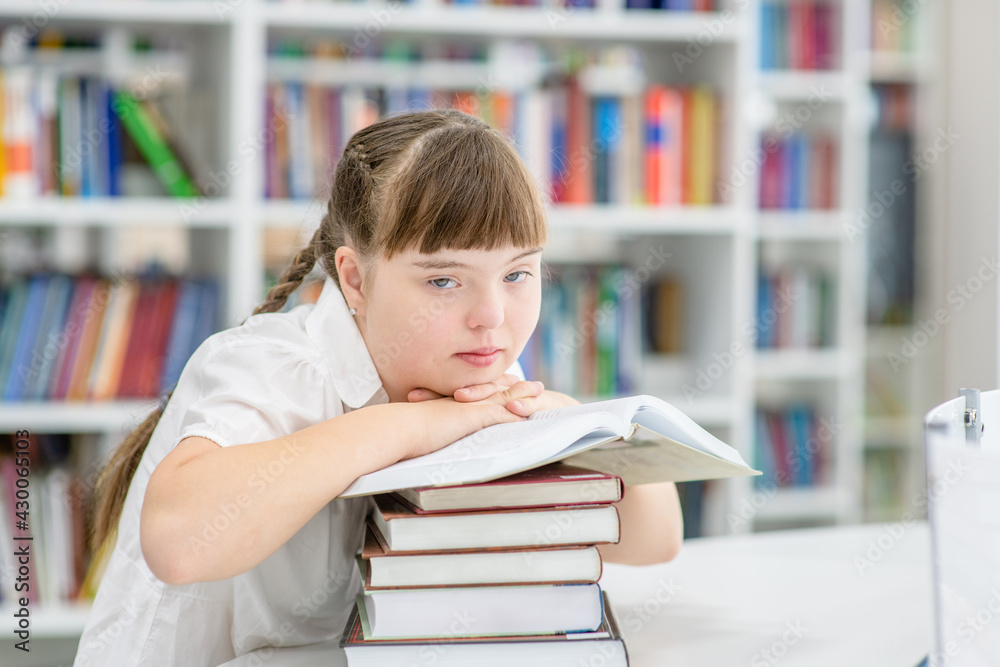 Thoughtful girl with syndrome down reads a book at library. Education for disabled children concept Thoughtful girl with syndrome down reads a book at library. Education for disabled children concept