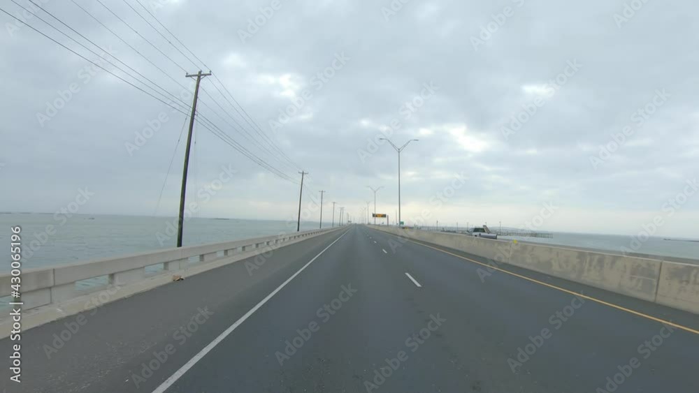 view thru rear window while driving on the JFK Memorial Causeway between North Padre Island and Corpus Christi Texas on a cloudy day; point of view view thru rear window while driving on the JFK Memorial Causeway between North Padre Island and Corpus Christi Texas on a cloudy day; point of view