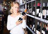 Ordinary middle aged woman looking for perfect wine for solemn occasion in wine store