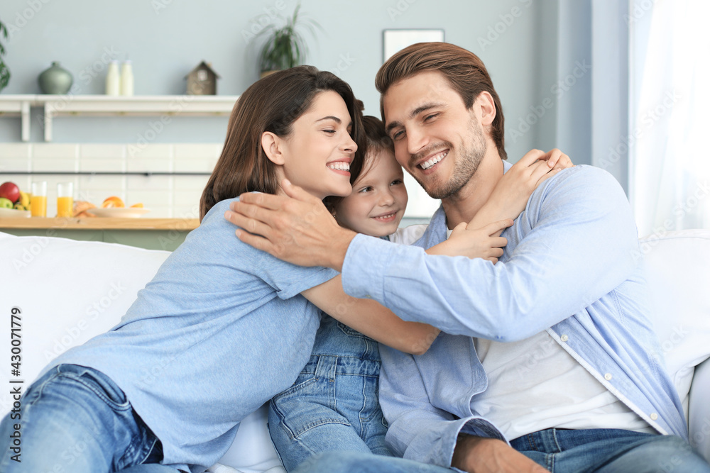 Positive friendly young parents with smiling little daughter sitting on sofa together while relaxing at home on weekend. Positive friendly young parents with smiling little daughter sitting on sofa together while relaxing at home on weekend.