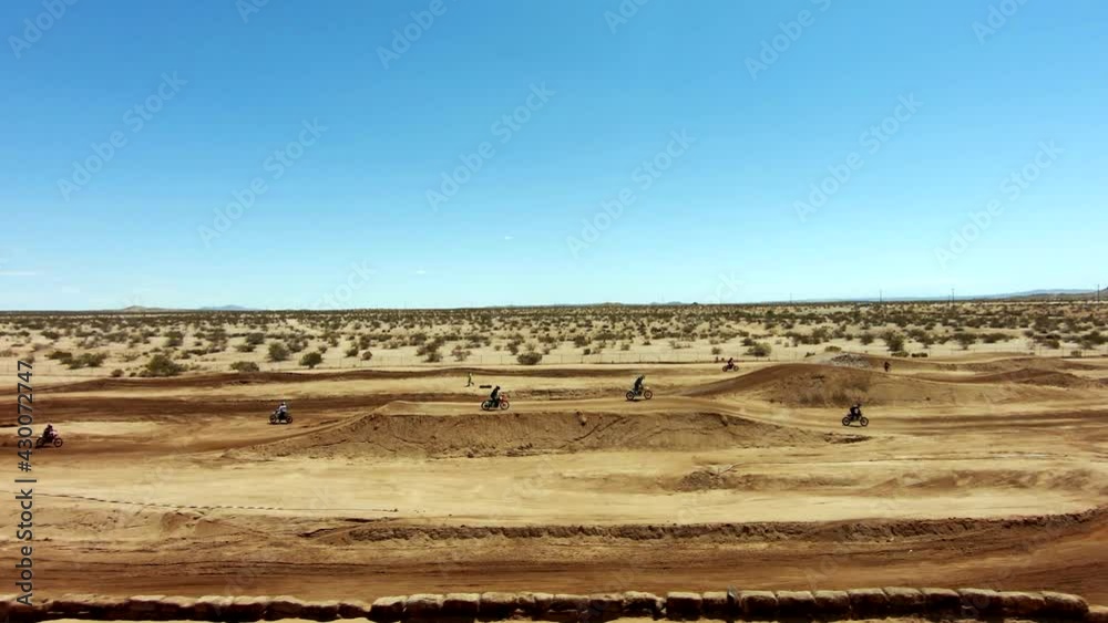 Motorcycles speed over jumps at a race track event in the desert - aerial slow motion view