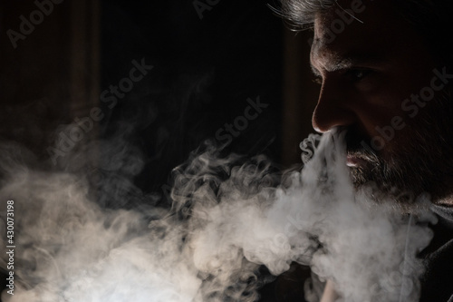 Profile view of a bearded mature man vaping against the light.