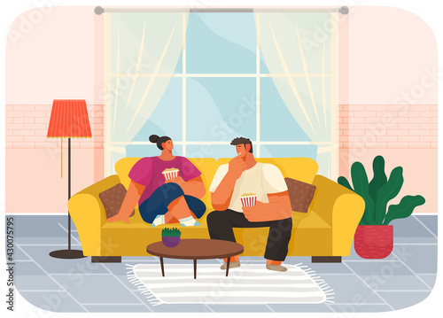 Couple sitting on couch at home in living room interior near big window, eating popcorn and talking. Family stay at home. Man and woman enjoy together, discuss movies. Young family spend time together