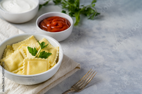 Ravioli with cheese with parsley and ketchup and sour cream on a light background with space for an inscription